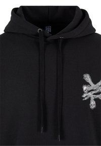 Sudadera negra de algodón con capucha forrada, presenta bordado de calavera y huesos cruzados en el lado derecho y cordones ajustables.