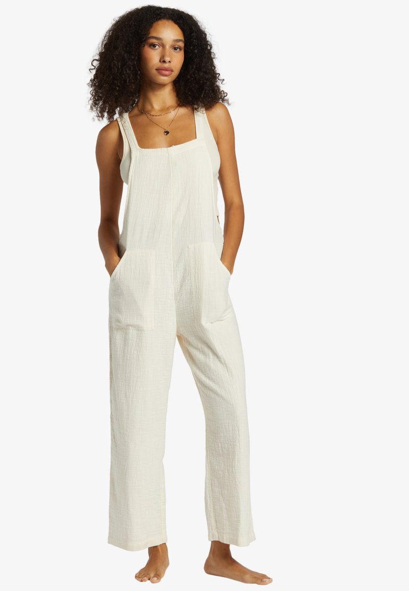 Jumpsuit color crema chiaro realizzato in tessuto testurizzato, con scollatura quadrata, spalline larghe, tasche laterali e un fit rilassato con gambe ampie.