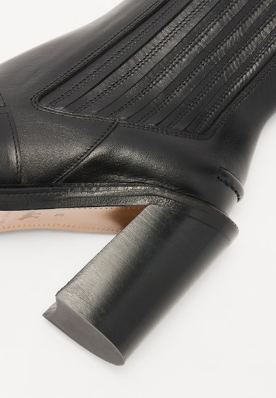Botín negro de cuero hasta el tobillo con pliegues verticales, puntera cuadrada y un tacón grueso y redondeado. Textura suave con detalles de costura sin costuras.