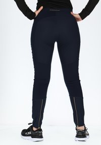 Leggings sportivi blu navy con design aderente, dotati di dettagli con cerniera dorata alle caviglie e vita alta. Materiale liscio e elasticizzato.