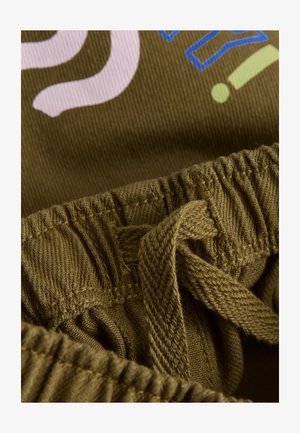 Olivově zelená látka s pasem na stažení; obsahuje barevný potisk textu v růžové a modré barvě. Texturovaný detail na pásku.