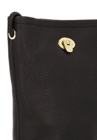 Zwarte leren tas met een gestructureerd oppervlak, voorzien van een sluiting en ronde hardware in goudkleur. Gladde bovenrand met gestikte details.