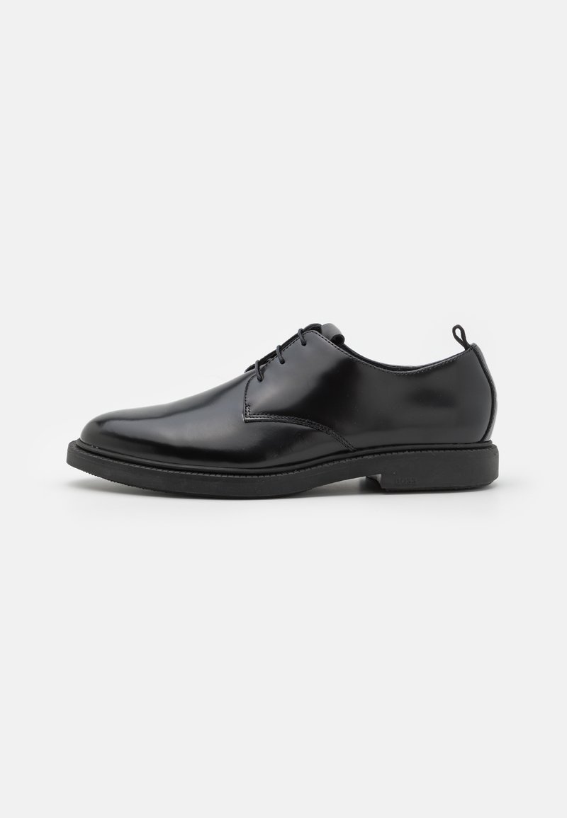 Scarpe eleganti in pelle nera lucida con lacci, tacco basso e linguetta sul retro, fotografate su uno sfondo chiaro e uniforme, vista laterale.