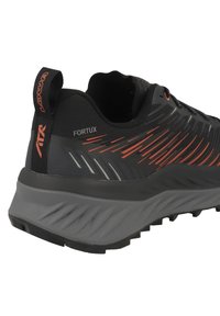Zwarte sportieve schoen met een gestructureerde bovenkant, rode accenten en een grijze zool. Voorzien van een trekhulp en een kenmerkend diagonaal streepdesign.