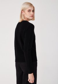 Schwarzer Pullover aus weichem Material mit rundem Halsausschnitt und geripptem Saum. Das Design hat lange Ärmel und eine lockere Passform.