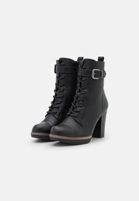 Stivali ankle in pelle nera con tacco alto a blocco, lacci frontali, una fascia e dettaglio fibbia in argento su sfondo bianco.