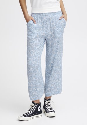 Lichtblauwe broek met bloemmotief, voorzien van een elastische tailleband, zijzakken en een losse pasvorm. Gemaakt met zwarte hoge sneakers.