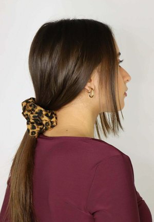 Gumka do włosów w panterkę, wykonana z tkaniny, trzymająca kucyk, o gładkiej fakturze. Nosi się ją z bordową bluzką, włosy ułożone starannie.