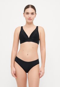 Melna mežģīņu bralette ar V veida dekoltē un platām siksnām, kas apvienots ar atbilstošiem melniem biksēm bikinia stilā ar viļņotu jostu.