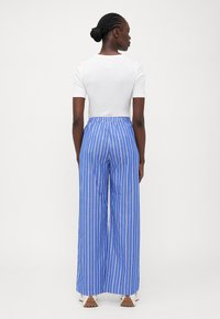 Blue and white striped wide-leg trousers with an elastic waistband, paired with a white fitted short-sleeve shirt. Textured fabric.