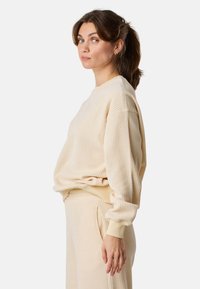 Beige geribbelde trui met lange mouwen en een ronde hals. Zachte textuur met aansluitende boorden en een ontspannen silhouet.