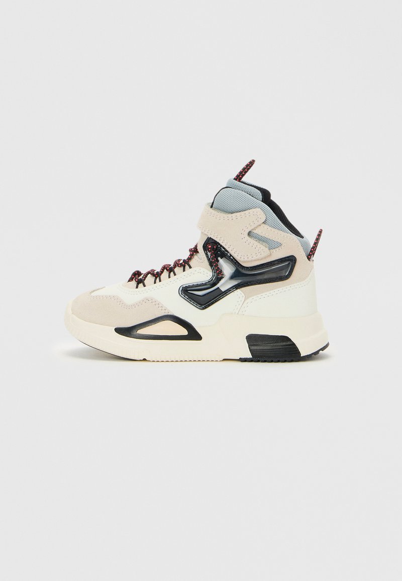 Zapatilla alta con un upper de ante en tonos beige y crema, con acentos en negro, suela texturada, cordones rojos y un collarín acolchado en el tobillo.