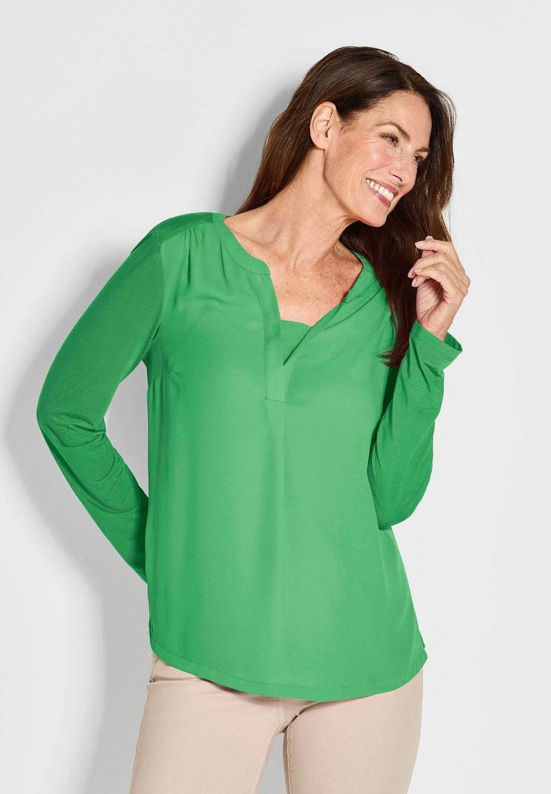 Grünes Langarmshirt mit V-Ausschnitt, gefertigt aus glattem Stoff. Verfügt über eine lockere Passform und einen abgerundeten Saum für Komfort und Stil.