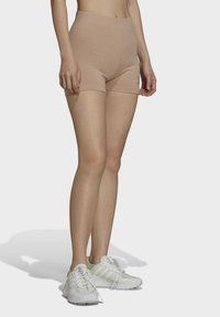 Shorts de sport beiges avec une taille haute et une texture lisse. Portés avec des baskets blanches à trois bandes et un design à bout rond.