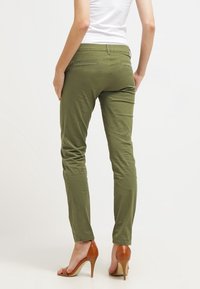 Pantaloni slim-fit verde oliva con una texture liscia, dotati di due tasche posteriori e vita a media altezza, abbinati a scarpe con tacco marroni.
