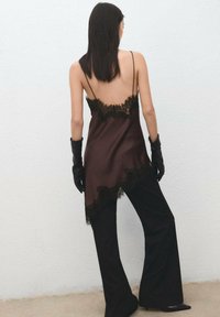 Camisola de satén marrón con ribete de encaje negro, combinada con pantalones negros acampanados y guantes negros. Textura suave y diseño de espalda descubierta.