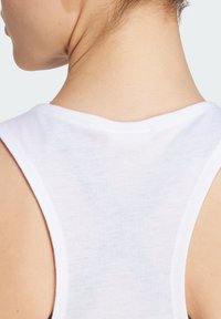 Débardeur blanc avec un col rond et des emmanchures larges, fabriqué dans un tissu doux et léger avec une texture lisse.