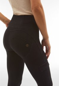 Leggings neri a vita alta in denim elastico con tasche posteriori curve e un accento del logo dorato. Texture liscia con un design aderente.