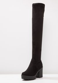 Stivale nero in faux suede alto fino al ginocchio con una piattaforma chunky e un alto tacco a blocco, caratterizzato da una superficie liscia e una punta arrotondata.