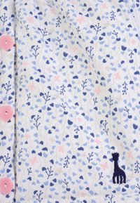 Tessuto bianco con un piccolo motivo floreale blu e rosa. Include bottoni rosa e un dettaglio di giraffa ricamato in blu navy. Trama morbida.