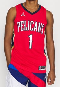 Red basketball jersey with "PELICANS" printed on the front, black accents, and a player number "1." Made of lightweight fabric with a mesh texture.
