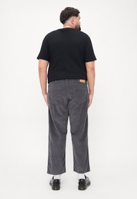 Grijze corduroy broek met wijde pijpen, een achterzak en een klein bruin label op de tailleband, gecombineerd met een zwart t-shirt met korte mouwen.