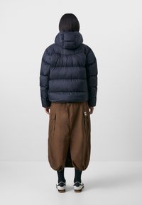 Navy puffer jacket with horizontal quilted sections and a hood, paired with a brown cargo skirt featuring large pockets and a split design.