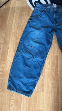 Modre jeans iz denima s sproščenim krojem, ravnimi hlačnicami in raztrganim robom. Vključujejo klasičen pet-pocket dizajn in označbo na pasu.