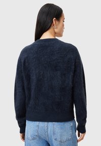 Navyblauer, flauschiger Pullover mit Rundhalsausschnitt und gerippten Bündchen, der eine weiche Textur und eine lässige Passform aufweist. Getragen mit hellblauen Jeans.
