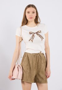 T-shirt blanc à manches courtes avec un design de noeud en imprimé léopard, associé à un short en khaki texturé et un petit sac rose avec une bandoulière en chaîne.