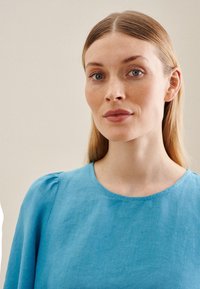 Top in lino azzurro chiaro con scollatura tonda e maniche a palloncino, caratterizzato da una trama morbida e dettagli di cucitura minimi.