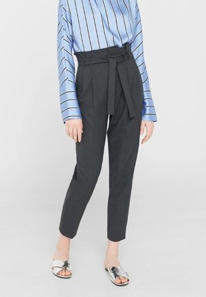 Woman wearing black high-waisted pants with a tied belt, a blue striped long-sleeve shirt, and silver open-toe slide sandals.