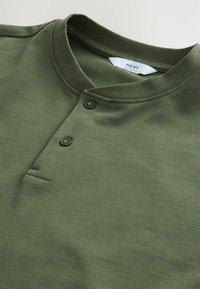 Olive green relaxed fit polo shirt made of soft cotton. Features a short placket with two buttons and a rounded collar design.