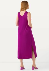 Fuchsia maxi-jurk met een ronde rug, mouwloos ontwerp, zijsplit en gemaakt van een gladde stof. Gecombineerd met blokhak roze muiltjes.