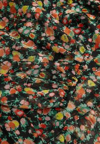 Tissu à motif floral présentant de petites roses dans des teintes de rouge, d'orange et de jaune sur un fond noir, avec une finition douce et texturée.