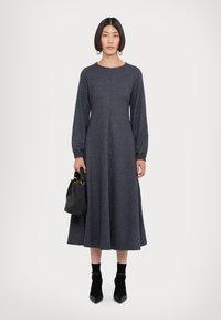 Abito in misto lana blu scuro, con maniche lunghe, collo rotondo e orlo svasato; abbinato a una borsa nera e tacchi neri a punta.