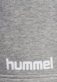 Grå bomullstyg med en mjuk textur, med en framträdande vit "hummel"-logotyp tryckt längs den nedre kanten. Enkelt och modernt design.