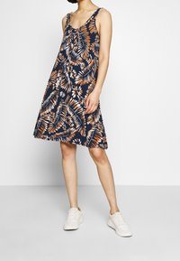 Robe A-line à imprimé floral en bleu marine, ornée de motifs de feuilles orange et blanches, avec de fines bretelles et une coupe décontractée. Assortie à des baskets blanches.