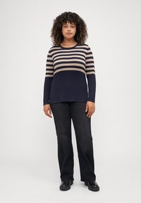 T-shirt à manches longues rayé en bleu marine et beige avec un col rond ; associé à un pantalon noir à jambe droite et des chaussures noires.