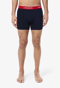 Námornícke modré boxerky vyrobené z elastickej bavlny s pásom s logom Lacoste v červenej farbe. Navrhnuté pre pohodlie, majú priliehavý strih a hladkú štruktúru.