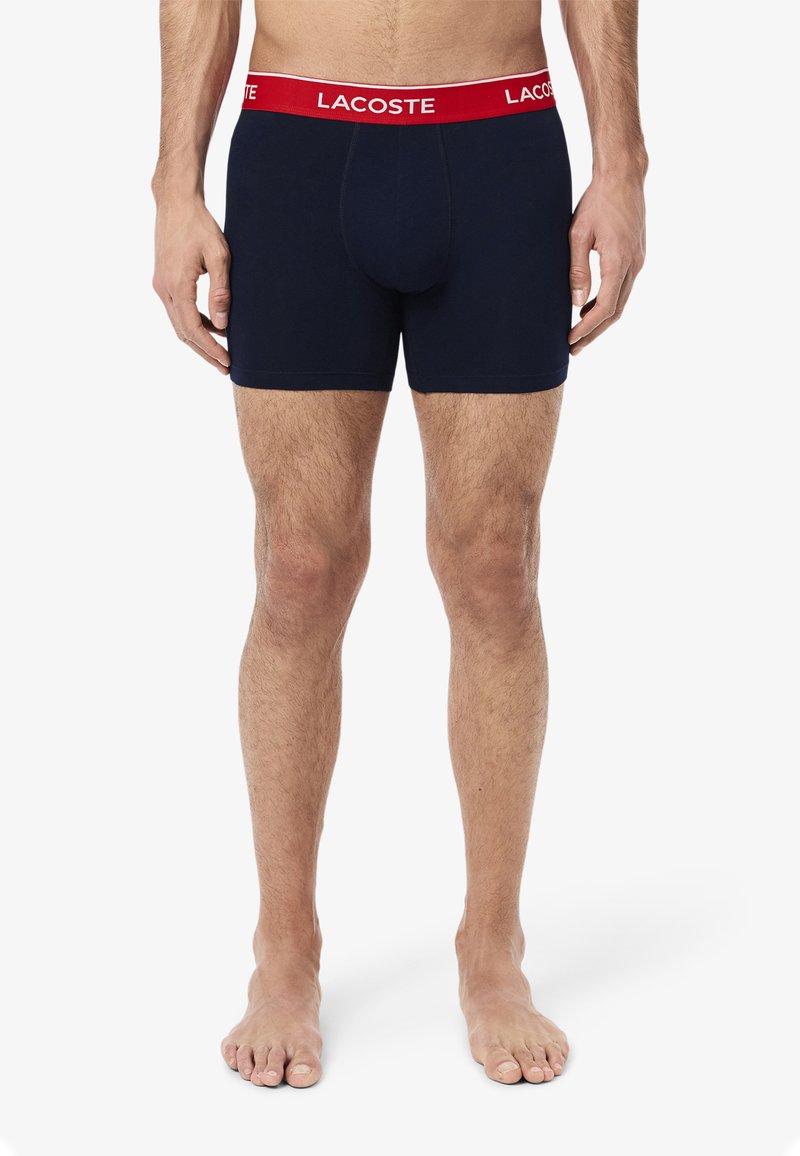 Námornícke modré boxerky vyrobené z elastickej bavlny s pásom s logom Lacoste v červenej farbe. Navrhnuté pre pohodlie, majú priliehavý strih a hladkú štruktúru.