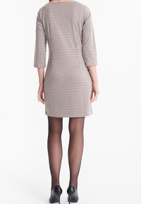 Rutig klänning i beige, röd och svart, med trekvartsärmar och en lätt A-linjeform. Bärs med genomskinliga svarta strumpbyxor och klackar.