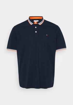 Tamsiai mėlynas polo marškinėlis iš medvilnės, su apykakle, kuri turi oranžines ir pilkas juosteles, trijų mygtukų užsegimą ir mažą siuvinėtą logotipą ant krūtinės.