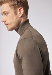 Maglione dolcevita marrone con un design aderente. Realizzato in materiale a maglia liscia. Presenta un colletto e cuciture a costine.