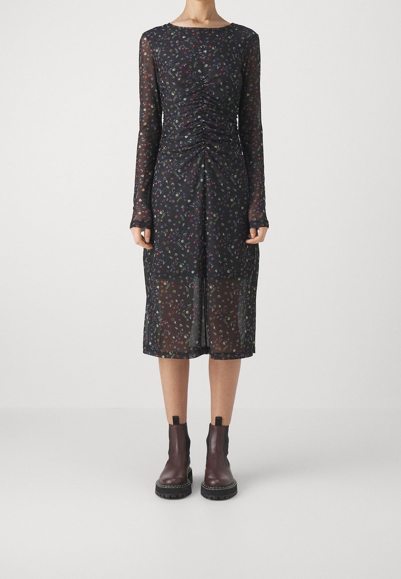 Musta pitkähihaisen mekko, jossa on värikäs kukkakuosi, rypytetty etupaneeli ja läpikuultava kangas. Yhdistetty ruskeisiin nilkkasaappaisiin, joissa on elastiset sivut.