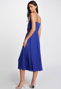 Vestido de tirantes en azul royal con cintura elástica y dobladillo a media longitud, hecho de una tela suave y fluida. Cuenta con un corte en la espalda.