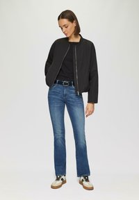 Zwarte bomberjack met rits, blauwe flared jeans en beige sneakers met zwarte accenten. Eenvoudig ontwerp, gladde textuur, casual uitstraling.