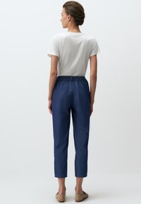 Biała koszulka z krótkim rękawem, casualowe niebieskie spodnie z elastycznym paskiem, krótkie, gładka tekstura, zestawione z beżowymi balerinami.