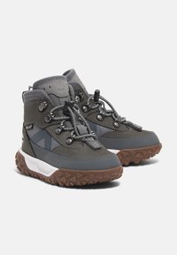 Šedé turistické boty s kombinací hladkých a strukturovaných materiálů, gumovými podrážkami s robustním vzorem, navržené pro dlouhou životnost.