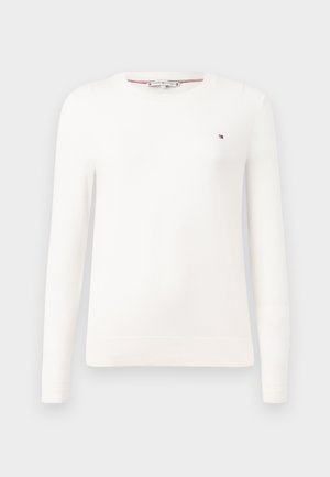 Baltas megztinis su apvalia iškirpte ir ilgomis rankovėmis. Ant krūtinės yra mažas logotipas, o rankovių ir apačios kraštai yra su raukšlėmis.